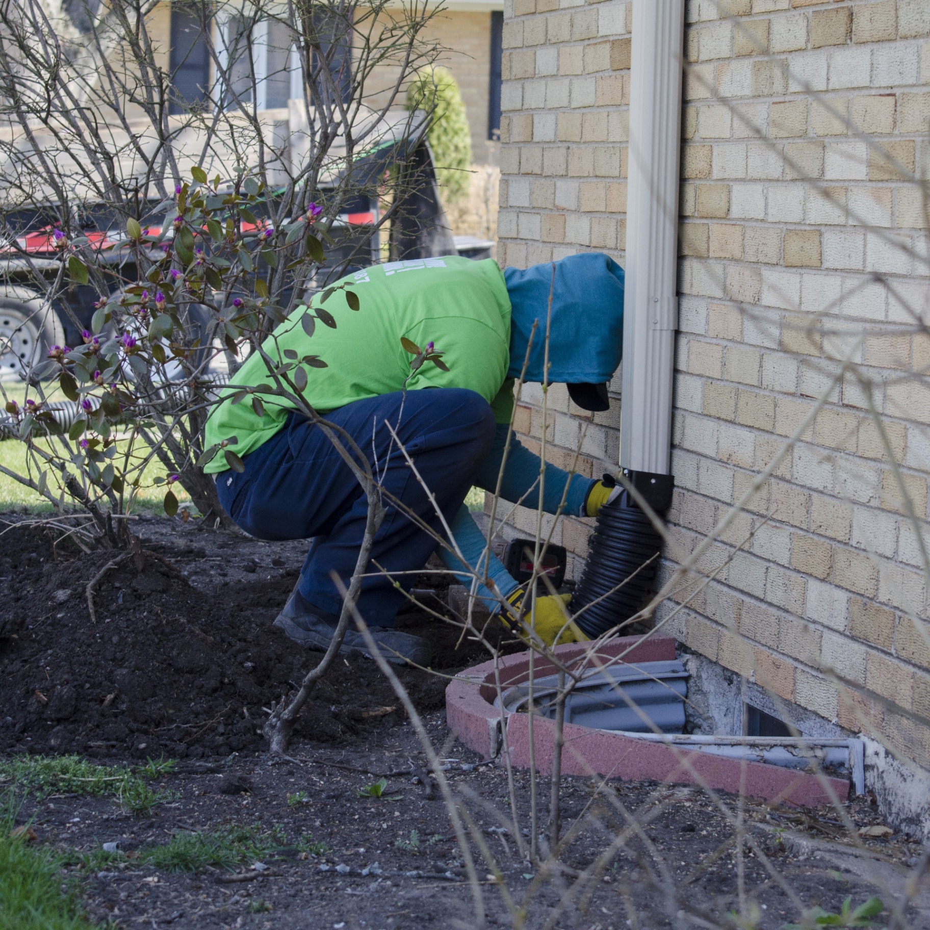 Revive Your Lawn crew installing downspout extension at brick foundation