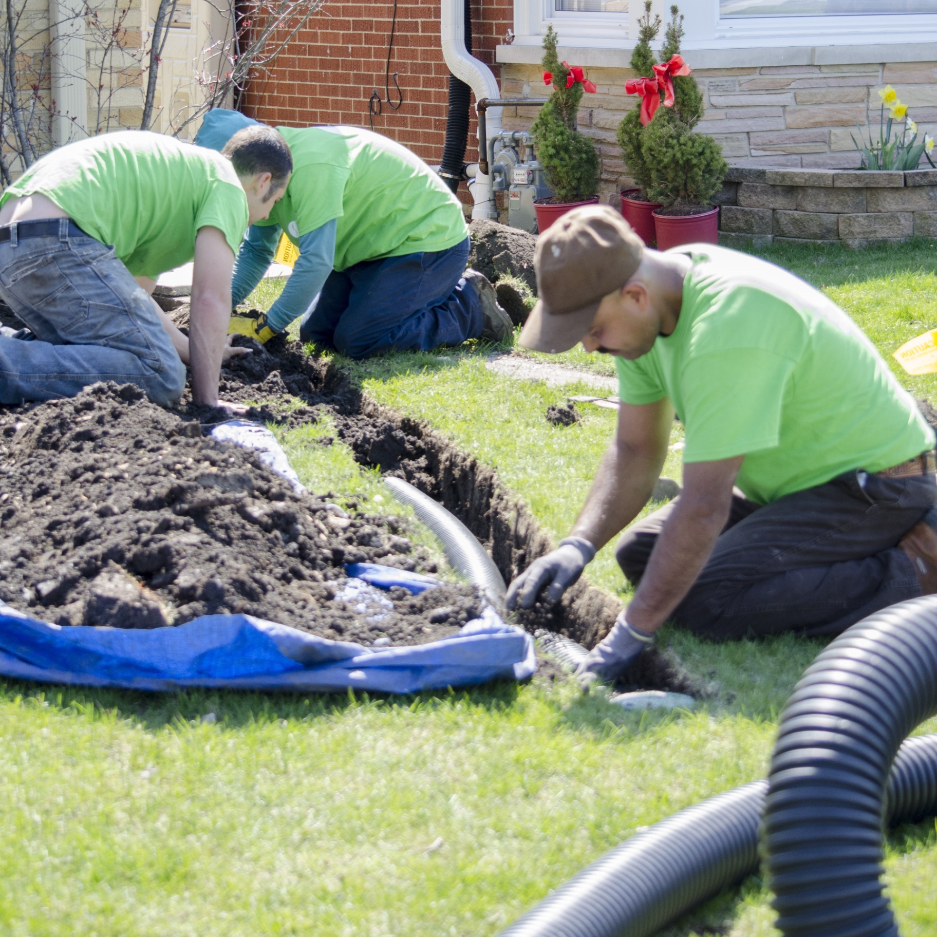 Revive Your Lawn crew hand-digging drainage trench next to home foundation