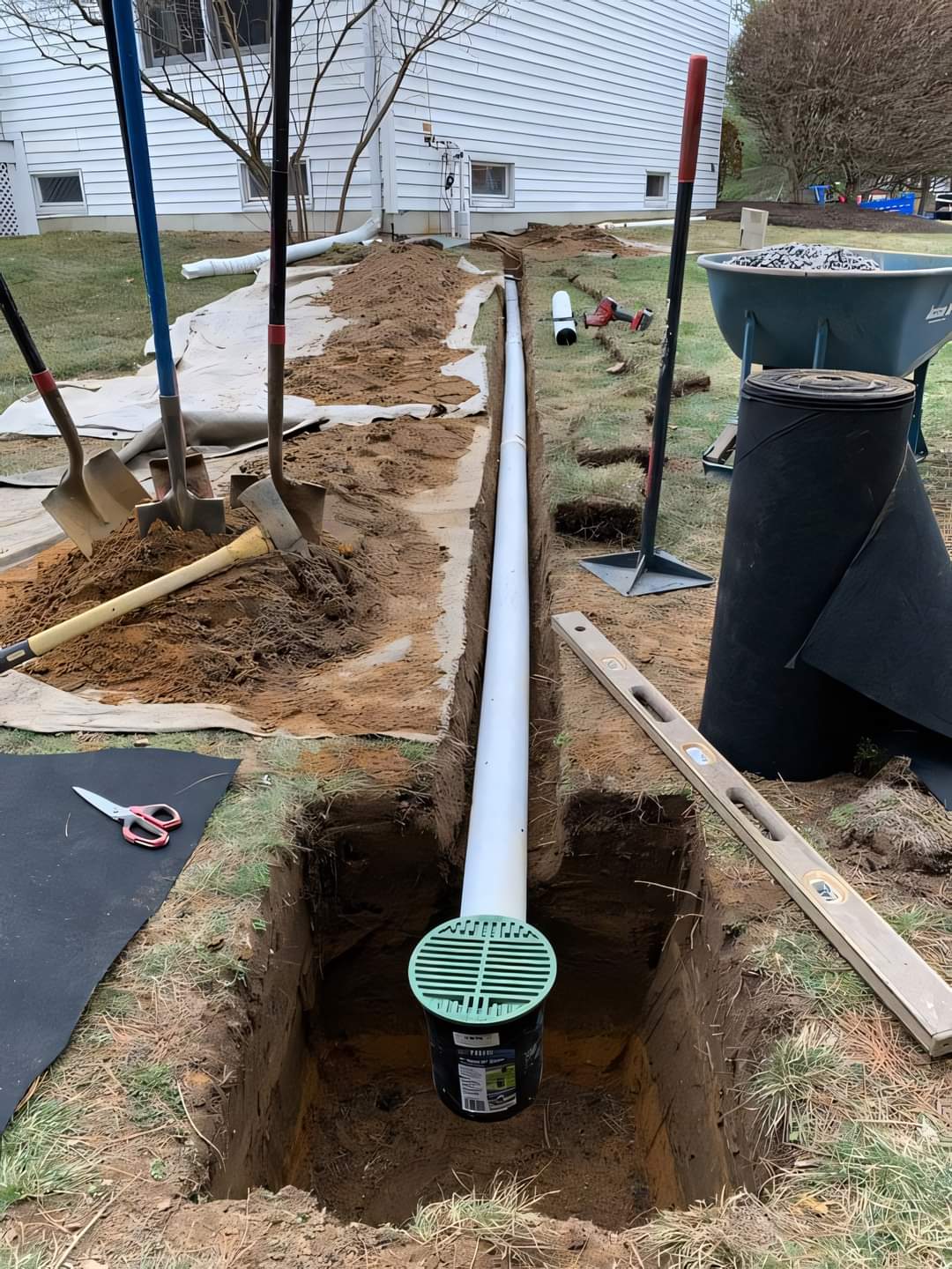 White PVC drain line running to pop-up emitter in backyard trench